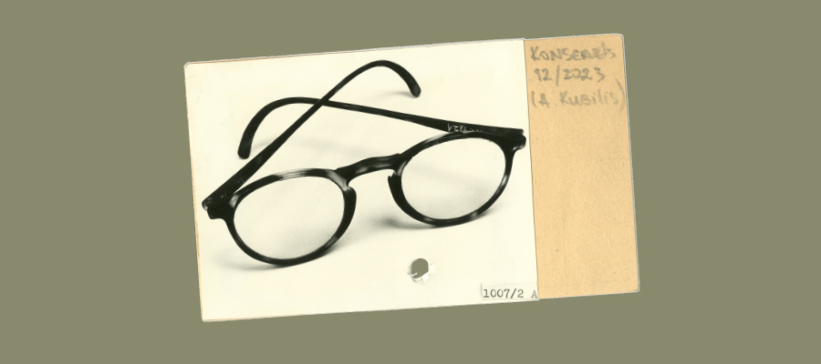 Black round glasses with thick lenses placed on an old, yellowed file with handwritten notes and date, 22/2003.