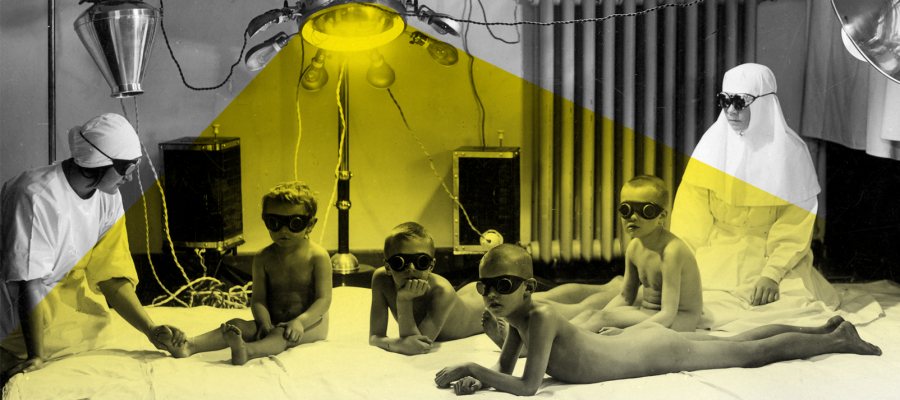 A doctor's office, where two nurses and four boys, all wearing glasses, are sitting on a mattress. A yellow light shines from a lamp above them.
