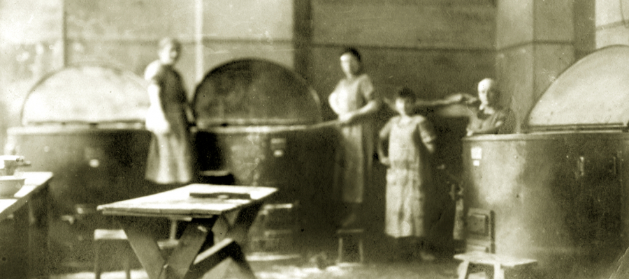 An old sepia picture of a kitchen with four people in it
