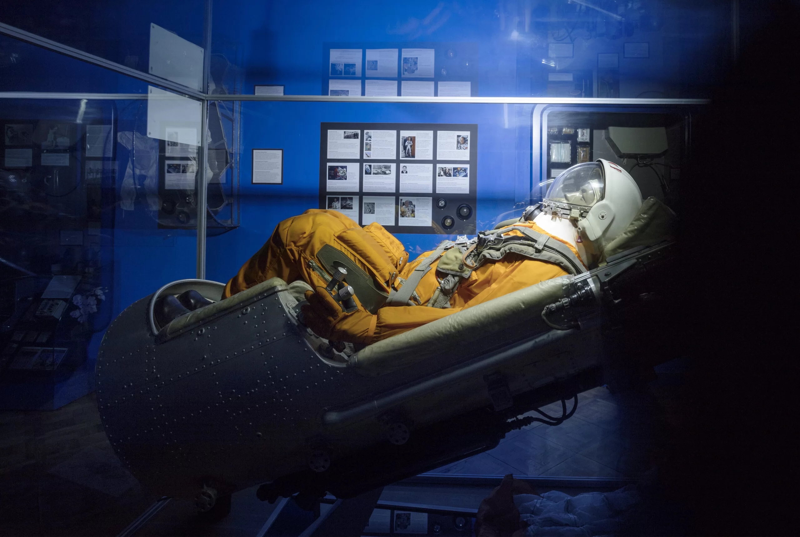 A photo from the museum's space exhibit showing a mannequin dressed as an astronaut on a chair. In the background are blue walls on which there are various informative tablets.