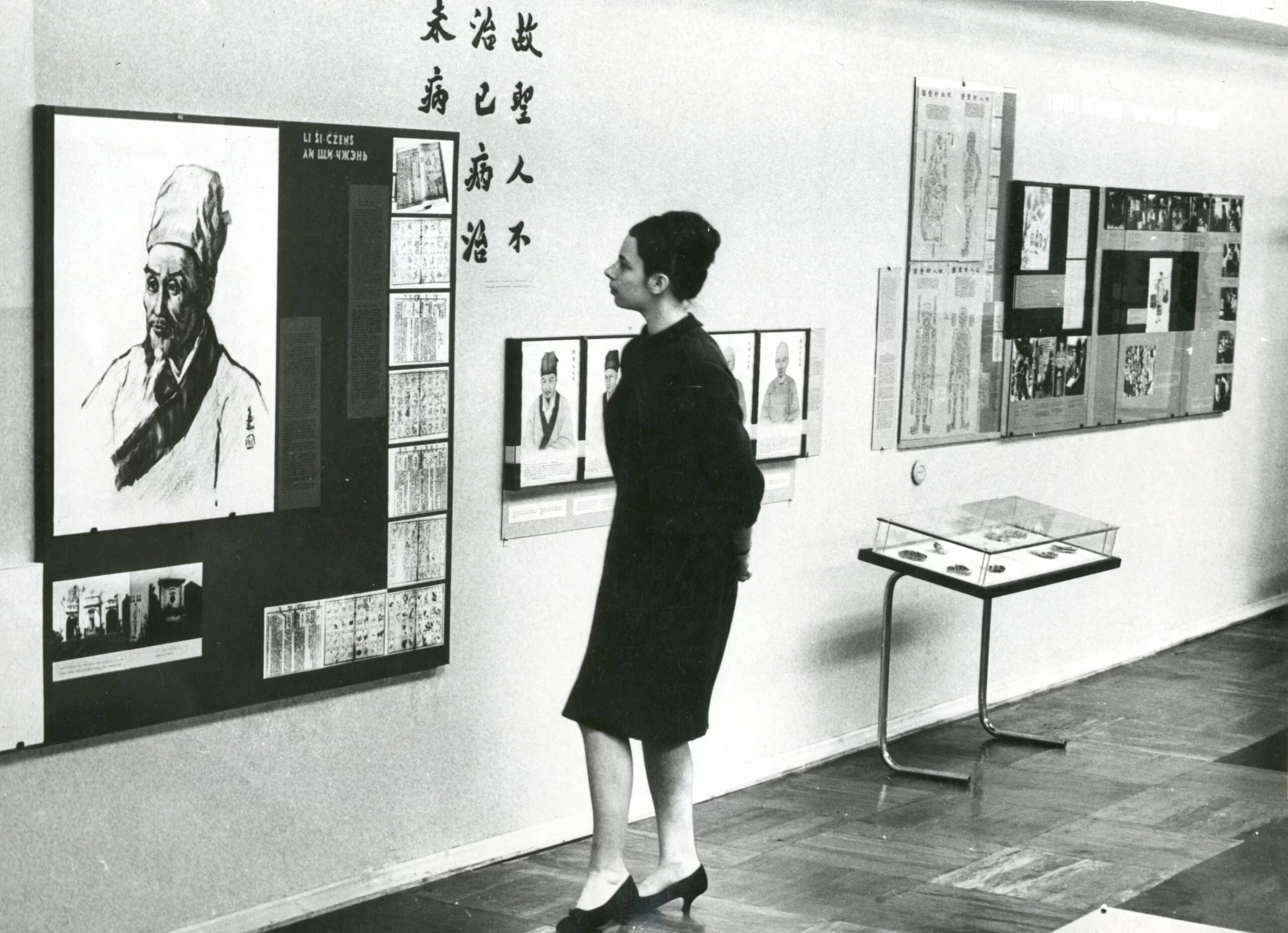 A woman walks through an exhibition about Chinese pharmaceuticals. There is a portrait of pharmacologist Li Shizhen and other related informative pictures and exhibits.
