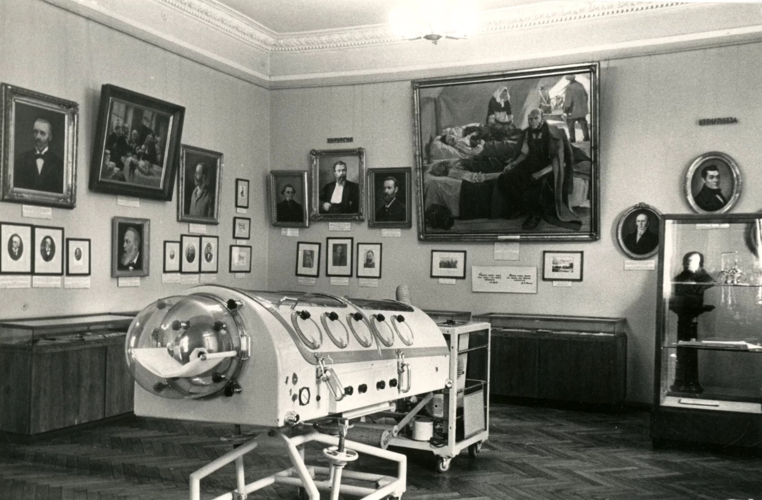 Photo of one of the museum exhibition rooms. Iron lungs can be seen in the middle, various display cases with exhibits are around, and many different pictures and paintings can be seen on the walls.