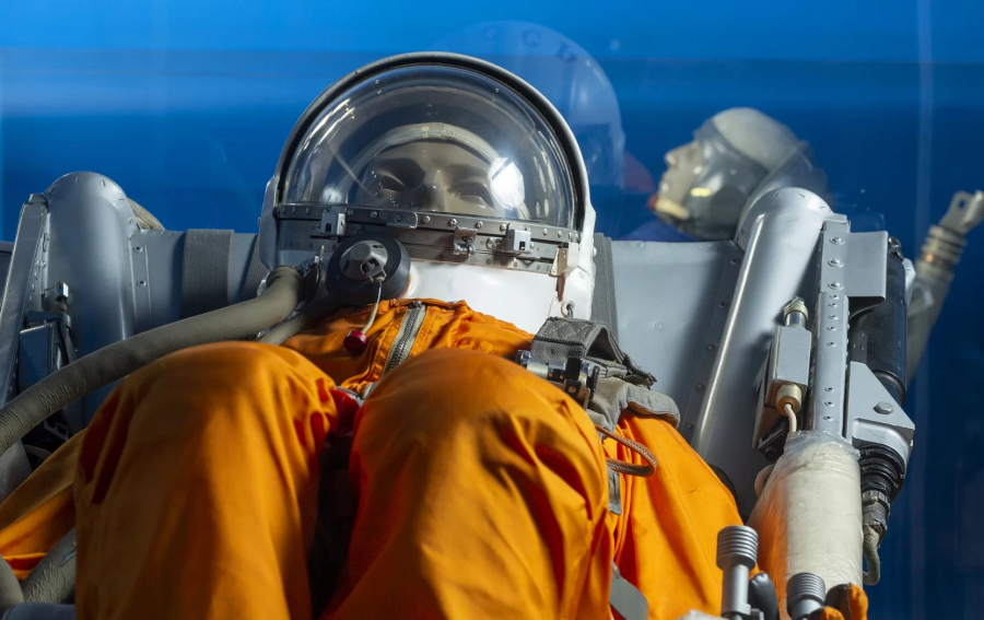 A spaceship’s suspension chair with a model with orange suit and breathing aid helmet in it
